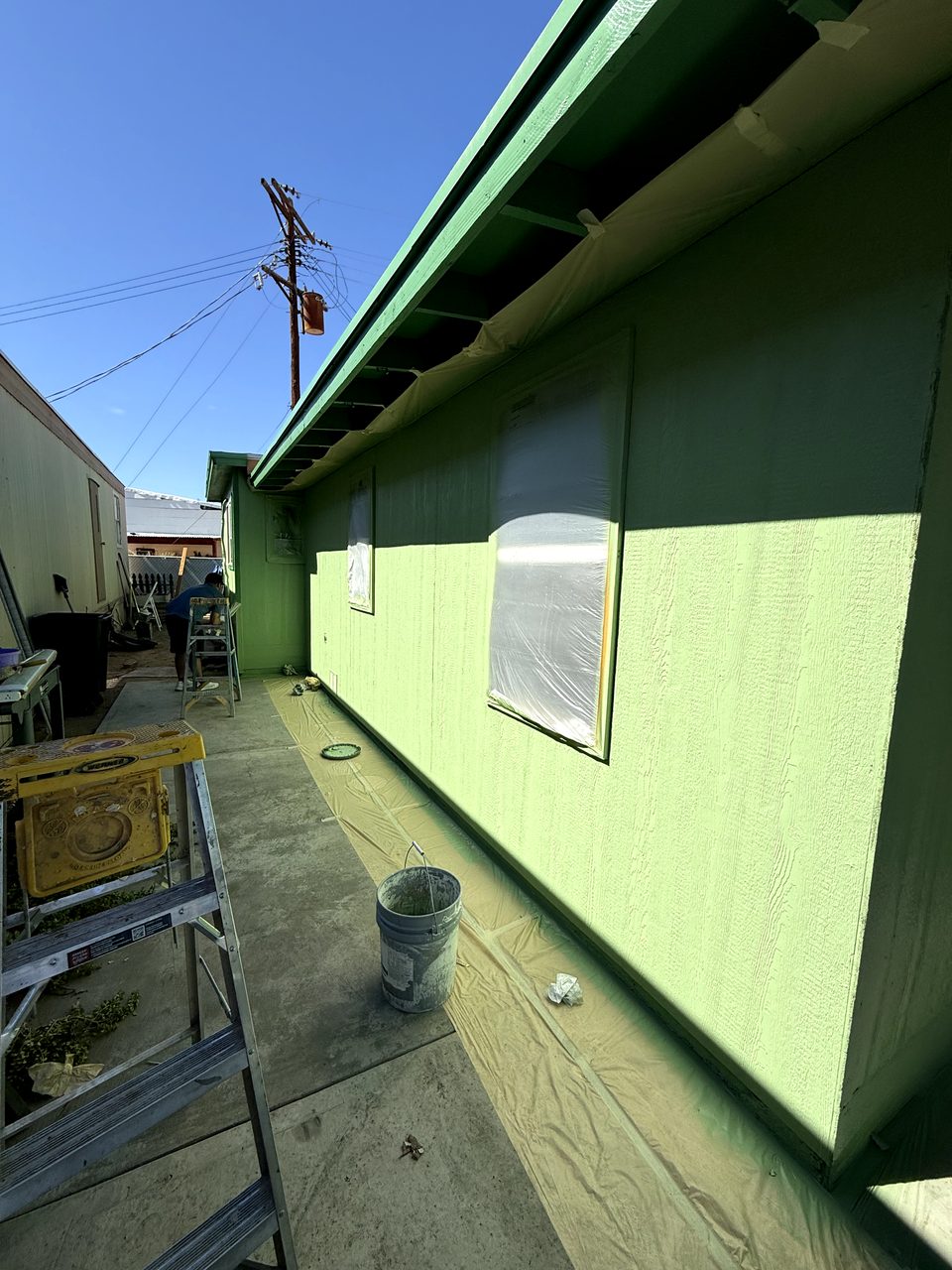 Windows masked with plastic and drop cloths down during a Phoenix metal-siding repaint