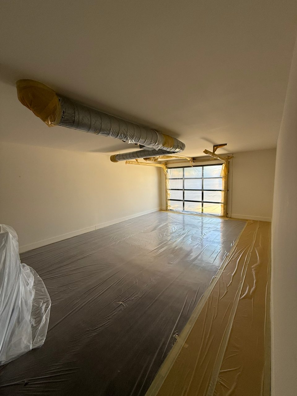 The exposed ductwork wrapped and the floors fully covered in plastic before spraying